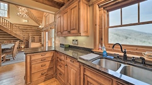 A spacious kitchen with wooden cabinets, a granite countertop, and a large window offering a view of the outdoors. - Hot Tub + Pool Table: Cozy Franklin Cabin! (Franklin)