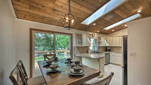 A dining area with a wooden table set for four, a wooden ceiling, and a view of a deck and trees outside. - Lake Nagawicka Home - 2 Blocks to Boat Launch (Delafield)