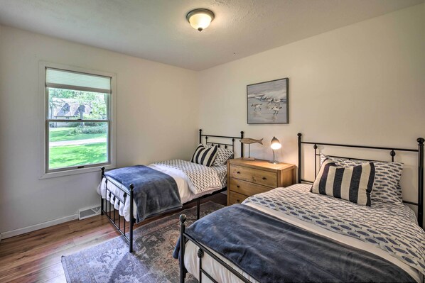 A bedroom with two single beds, a nightstand, a lamp, a window with blinds, and a painting on the wall.