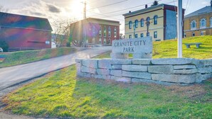 A stone sign reading "Granite City Park" with a road leading to a building with arched windows. - Cozy Water-view Apt in the Heart of Downtown! (Hallowell)