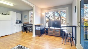 A modern kitchen with white cabinets, a dining area with a wooden table and chairs, and a large window with a view of trees. - Cozy Water-view Apt in the Heart of Downtown! (Hallowell)