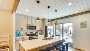 A modern kitchen with white cabinets, stainless steel appliances, a large island with bar stools, and pendant lighting. - Spacious Townhome ~ 7 Mi to Deer Valley Resort! (Heber City)