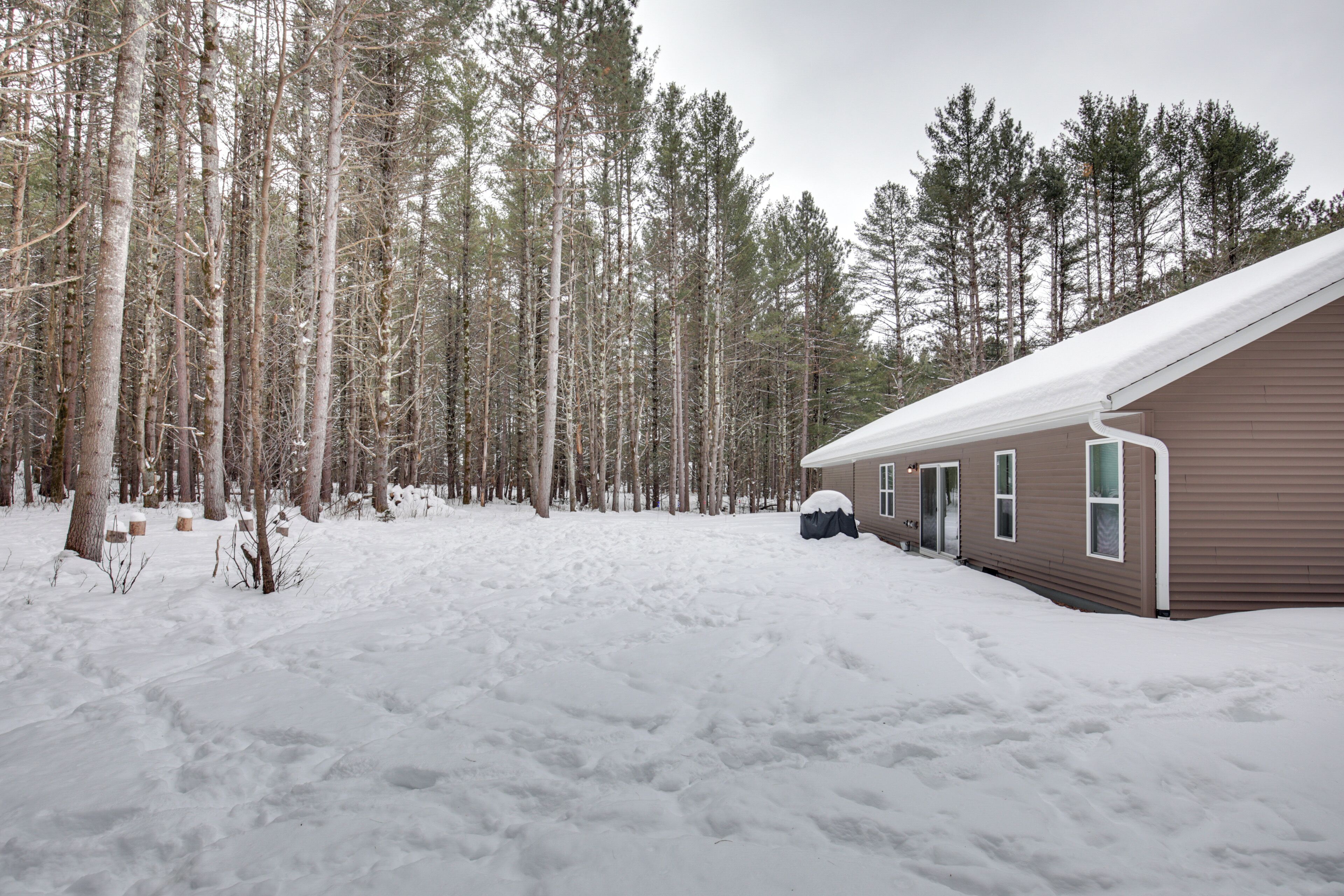 Une cabane au cœur d’une forêt enneigée, avec un toit recouvert de neige et un ciel dégagé.