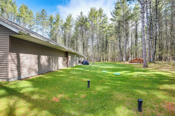 A house with a covered porch, a well-maintained lawn, and a stack of firewood in the yard. - Pet-friendly Woodruff Cabin Near Lakes (Woodruff)