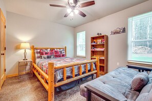 Een slaapkamer met een houten bed, een nachtkastje met een lamp, een boekenkast en een raam met jaloezieën.
