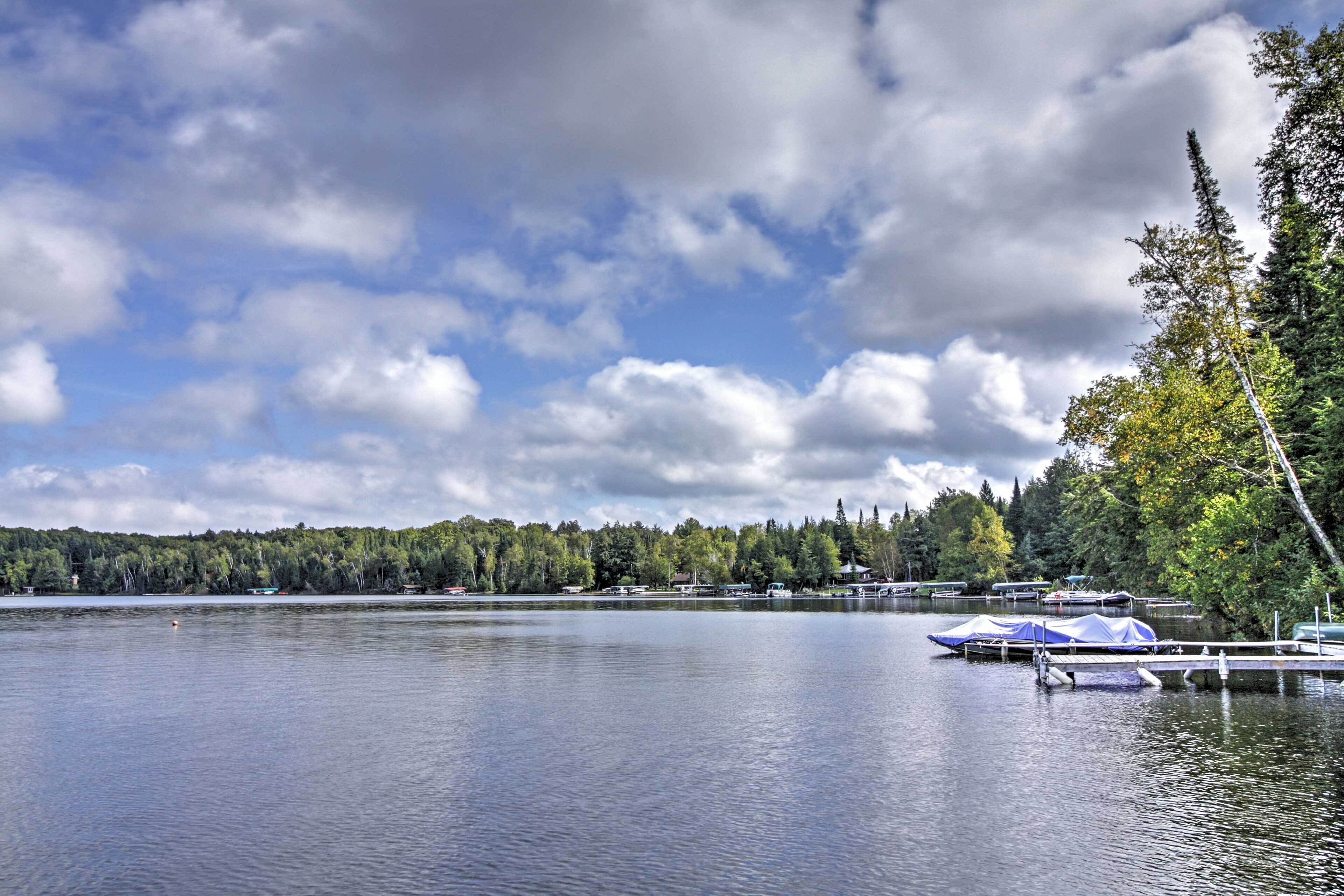 A calm lake with boats docked, surrounded by trees and a cloudy sky.