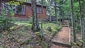 Eine Hütte, umgeben von dichtem Wald, mit einer Holzterrasse und einem Feldweg, der zum Eingang führt.