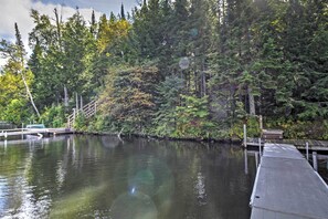 Un lago tranquilo con un muelle de madera que se adentra en el agua, rodeado de un denso bosque.