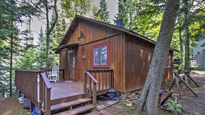 Ein rustikales Blockhaus mit einer Holzdiele und einer kleinen Veranda, umgeben von Bäumen.
