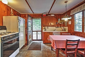 Cocina de cabaña con paredes de madera, un refrigerador, estufa y una mesa de comedor con sillas.