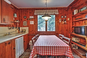 L’intérieur d’un chalet en bois, avec une table à carreaux, des armoires en bois, une fenêtre donnant sur les arbres et un luminaire suspendu.