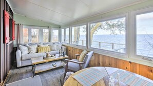 Ein gemütliches Zimmer mit Sofa, Sessel und Tisch, großen Fenstern mit Blick auf das Wasser und Holzwänden.