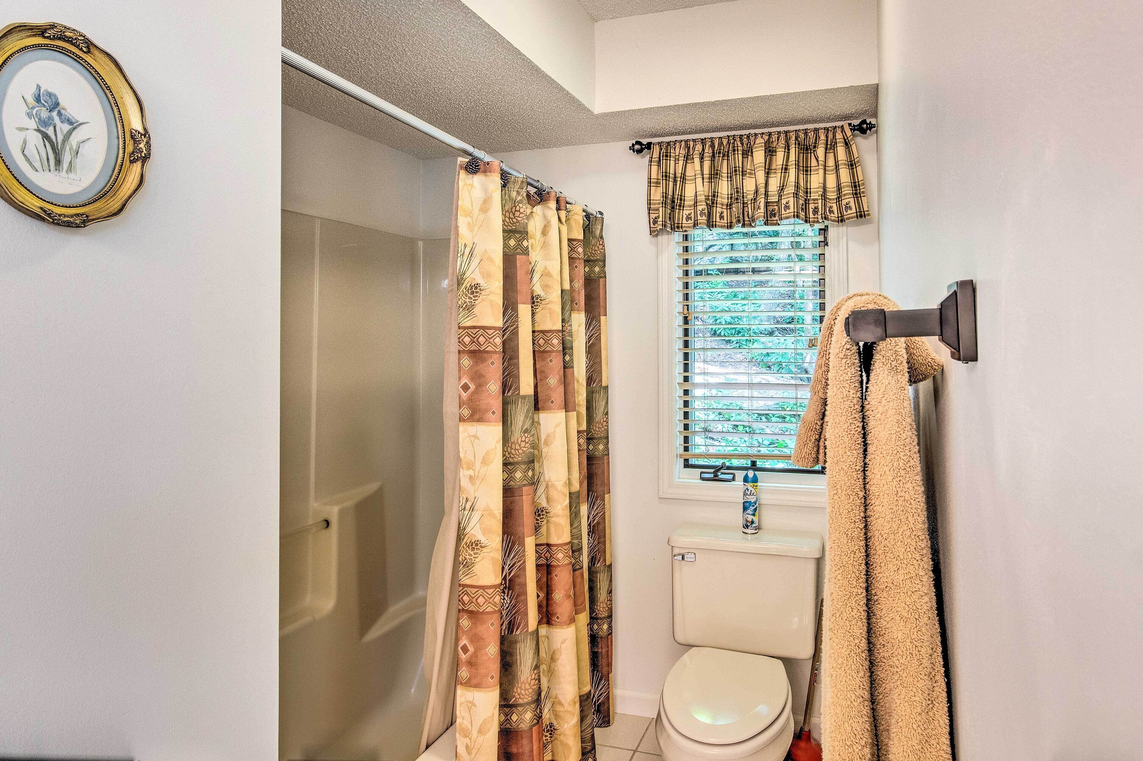 A bathroom with a shower curtain, a toilet, a window with blinds, and a towel rack.