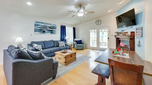 A living room with a sofa, a wooden coffee table, a dining table, and a TV mounted on the wall. - Lakefront Home w/ Kayaks & Dock in Hot Springs! (Hot Springs)