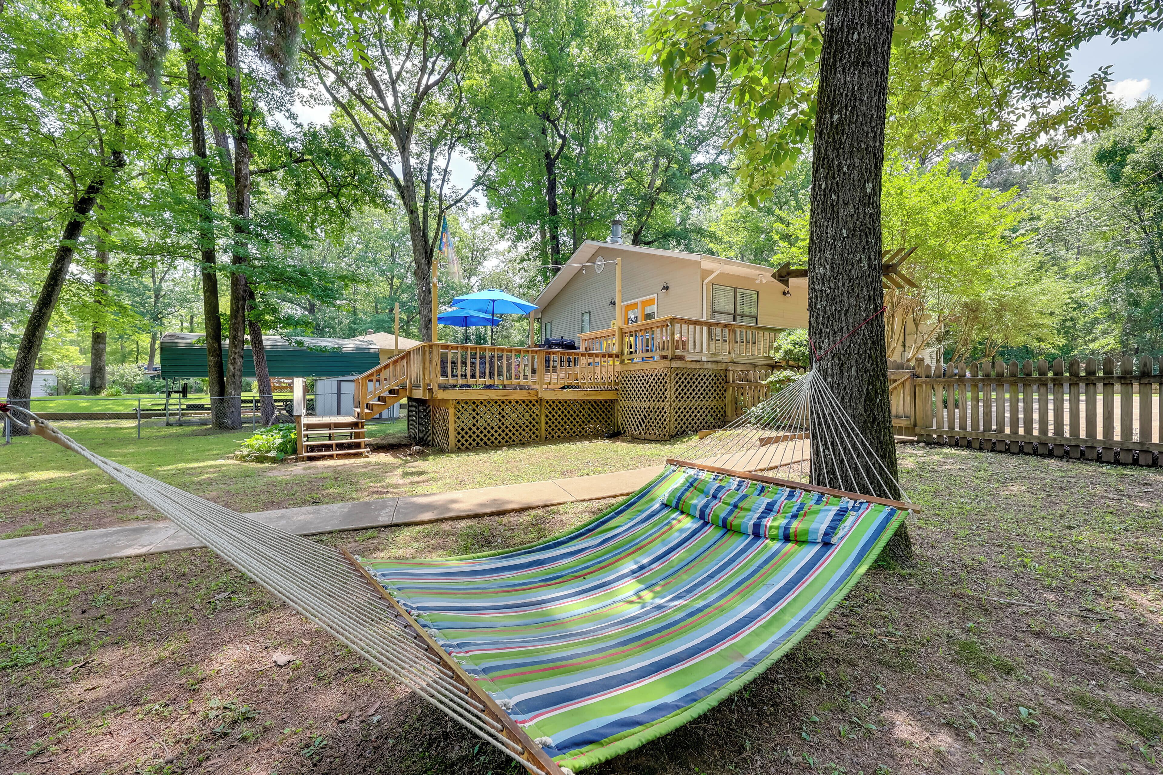 A hammock in a wooded area with a wooden deck and a house in the background.