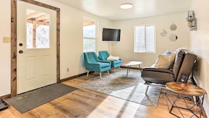 Une pièce avec une porte en bois, deux fauteuils turquoise, un canapé en cuir marron, une petite table ronde et un téléviseur fixé au mur.