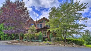 A two-story house with a stone facade, a wooden deck, and a well-maintained garden with various shrubs and trees. - River Access & Game Room: Piney Creek Cabin! (Piney Creek)