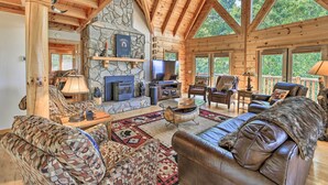A spacious living room with a stone fireplace, leather sofas, and a large TV. - River Access & Game Room: Piney Creek Cabin! (Piney Creek)