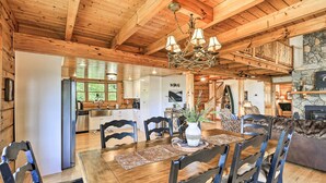 A wooden interior with a dining table, chairs, a chandelier, and a stone fireplace. - River Access & Game Room: Piney Creek Cabin! (Piney Creek)