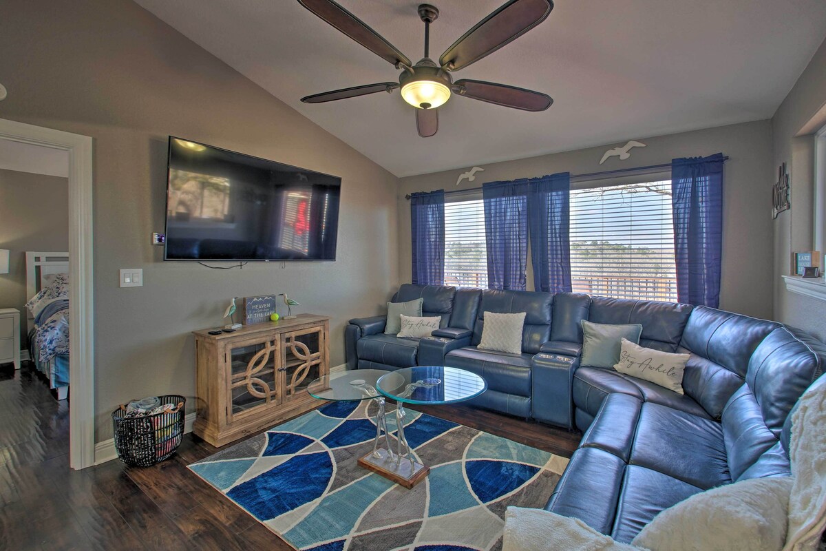 A living room with a leather sofa, a glass coffee table, a ceiling fan, a flat-screen TV, and a window with curtains.