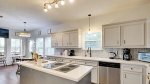 A modern kitchen with white cabinetry, a central island with a built-in stove, and a dishwasher.