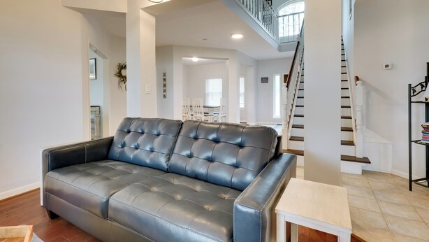 A spacious living room with a dark leather sofa, a wooden coffee table, and a staircase leading to an upper floor.