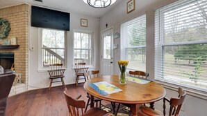 A dining room with a wooden table, six chairs, a chandelier, and a fireplace.