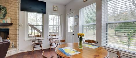 A dining room with a wooden table, six chairs, a chandelier, and a fireplace.