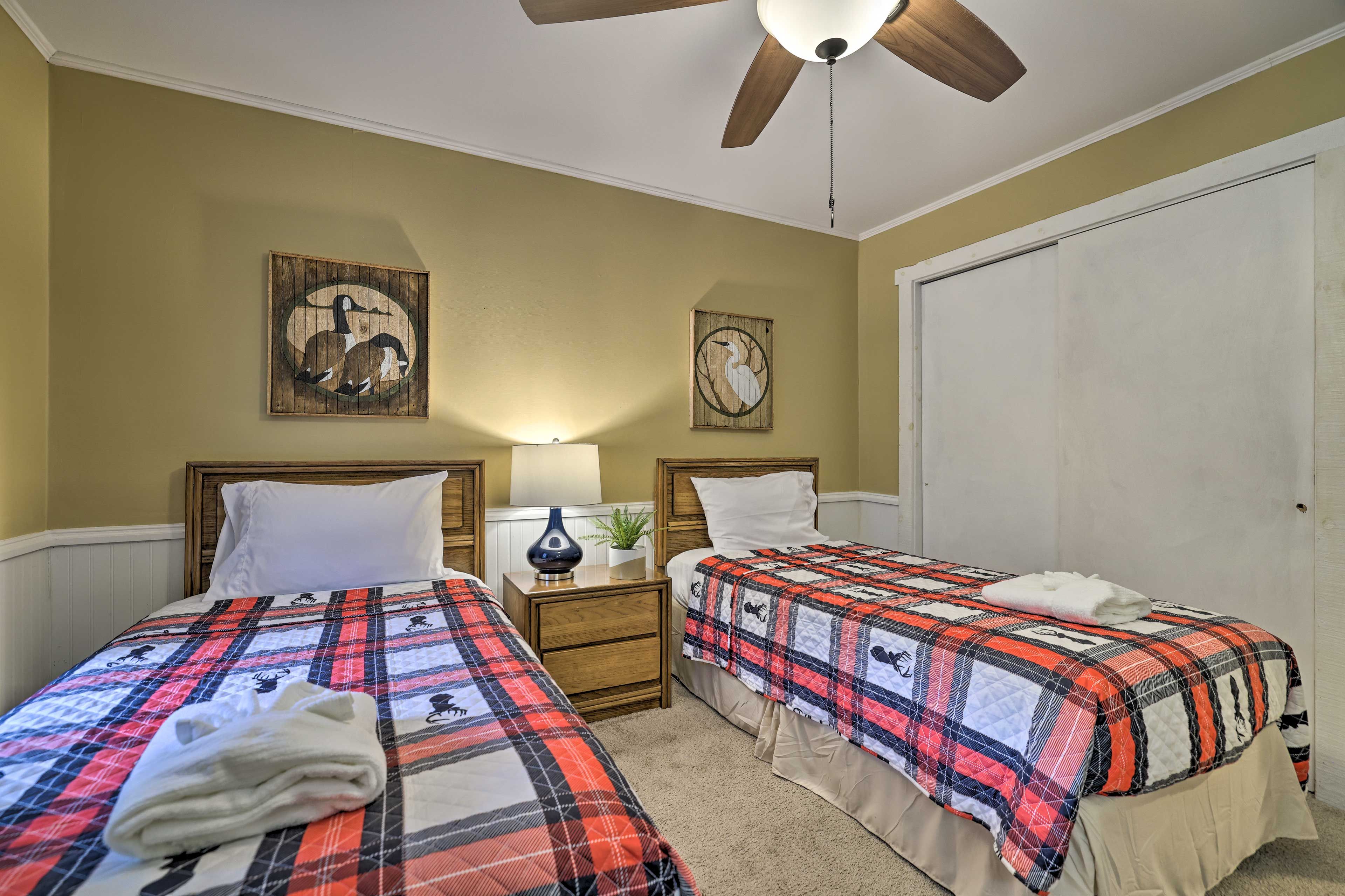 A bedroom with two beds, a ceiling fan, and wall art.