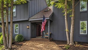 A modern two-story house with a dark exterior, a front porch, and an American flag. - Poconos Retreat By Jack Frost Wooded Escape (White Haven)