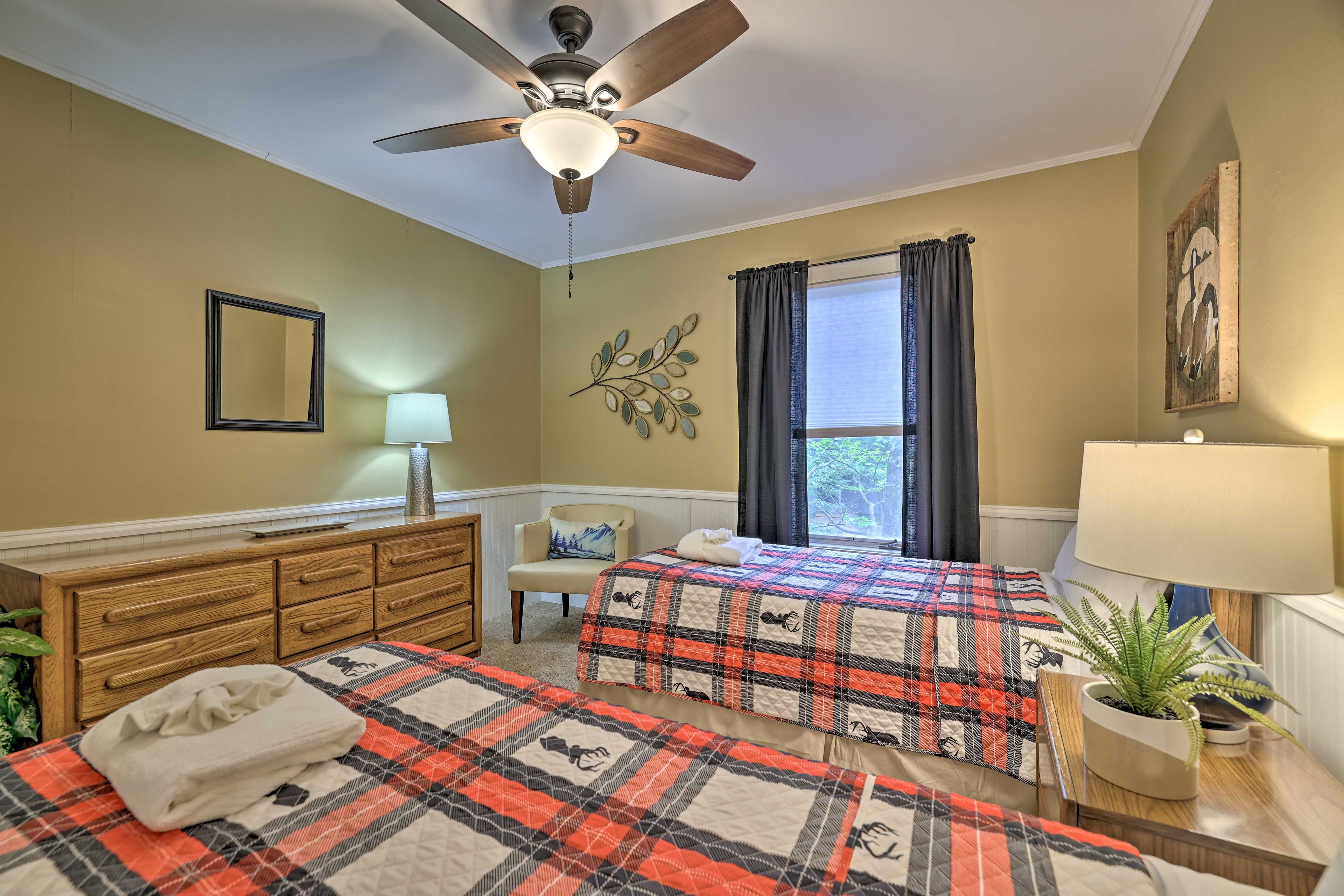 A bedroom with two beds, a ceiling fan, a dresser, a chair, a window with curtains, and a plant on a nightstand.