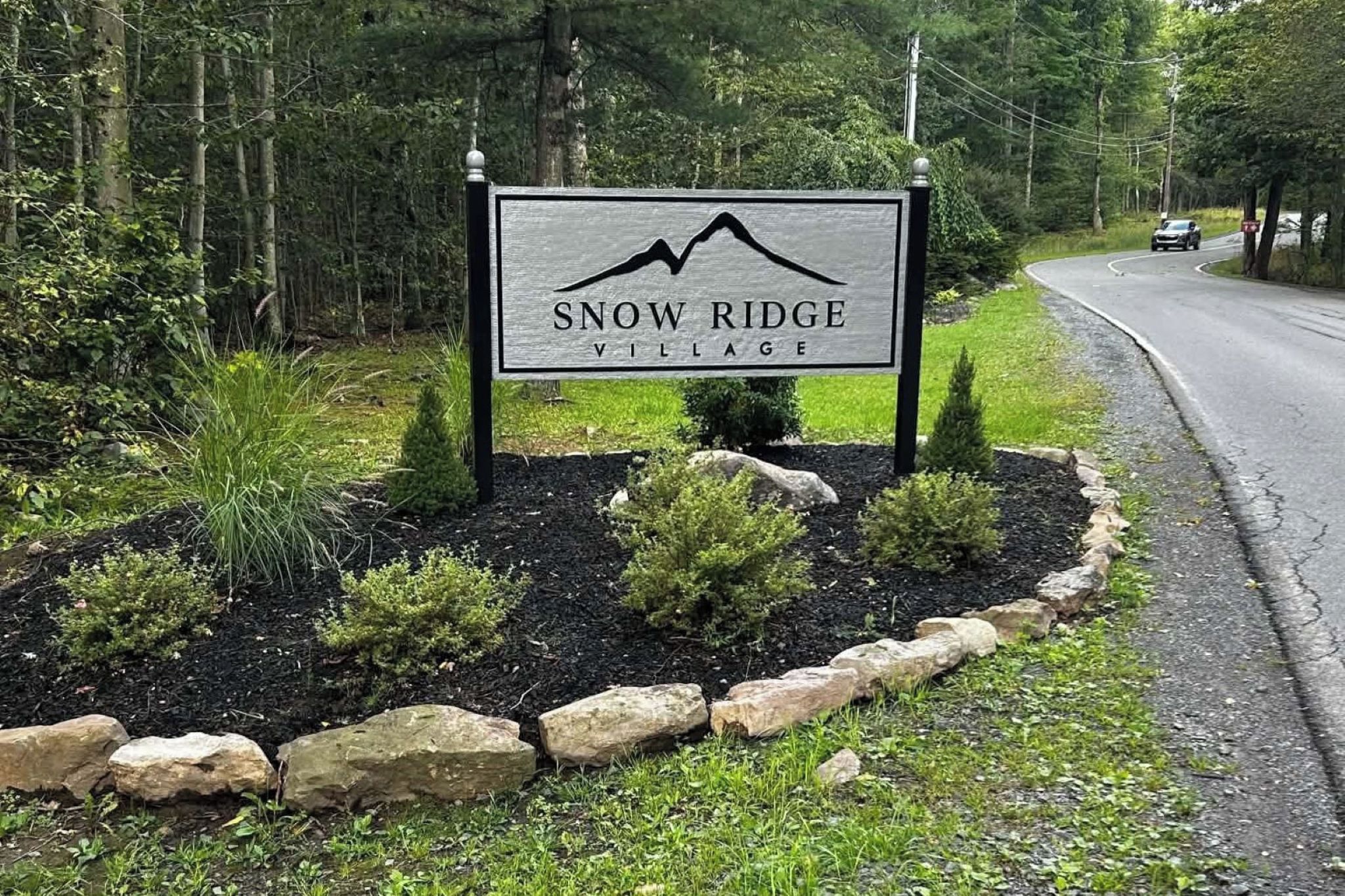 Schild für Snow Ridge Village mit einer angelegten Grünfläche mit Steinen und Sträuchern.