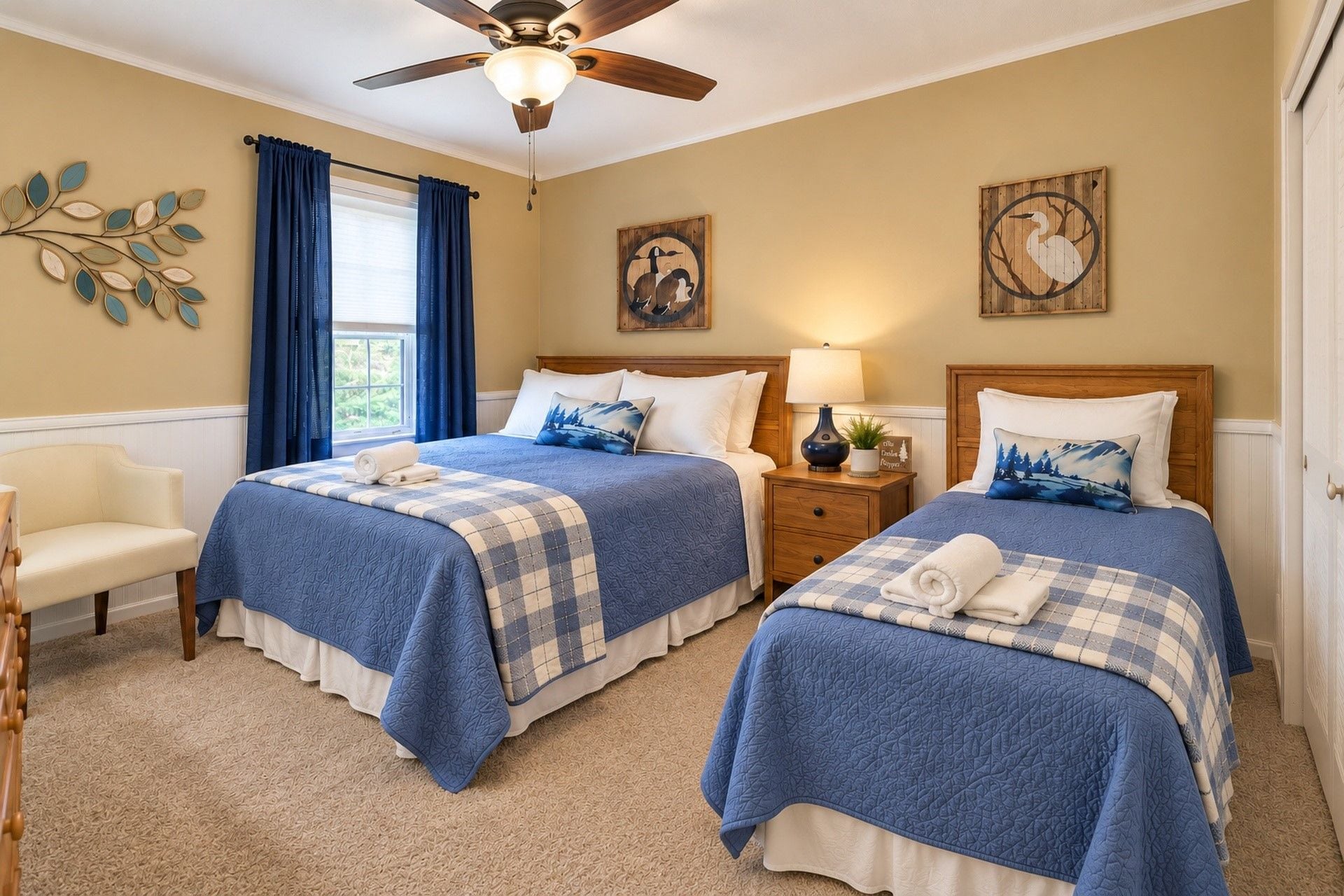 A hotel room with two beds, a ceiling fan, a window with curtains, and wall art.