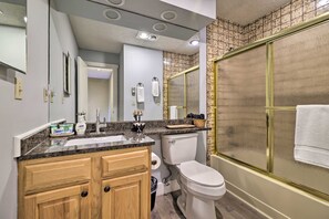 A modern bathroom with a granite countertop, wooden cabinets, a toilet, a shower with a glass door, and a large mirror. - Poconos Retreat by Jack Frost Wooded & Peaceful (White Haven)