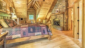 Ein Schlafzimmer in einer Blockhütte mit einem hölzernen Bett, einem Steinkamin und einem Deckenventilator.