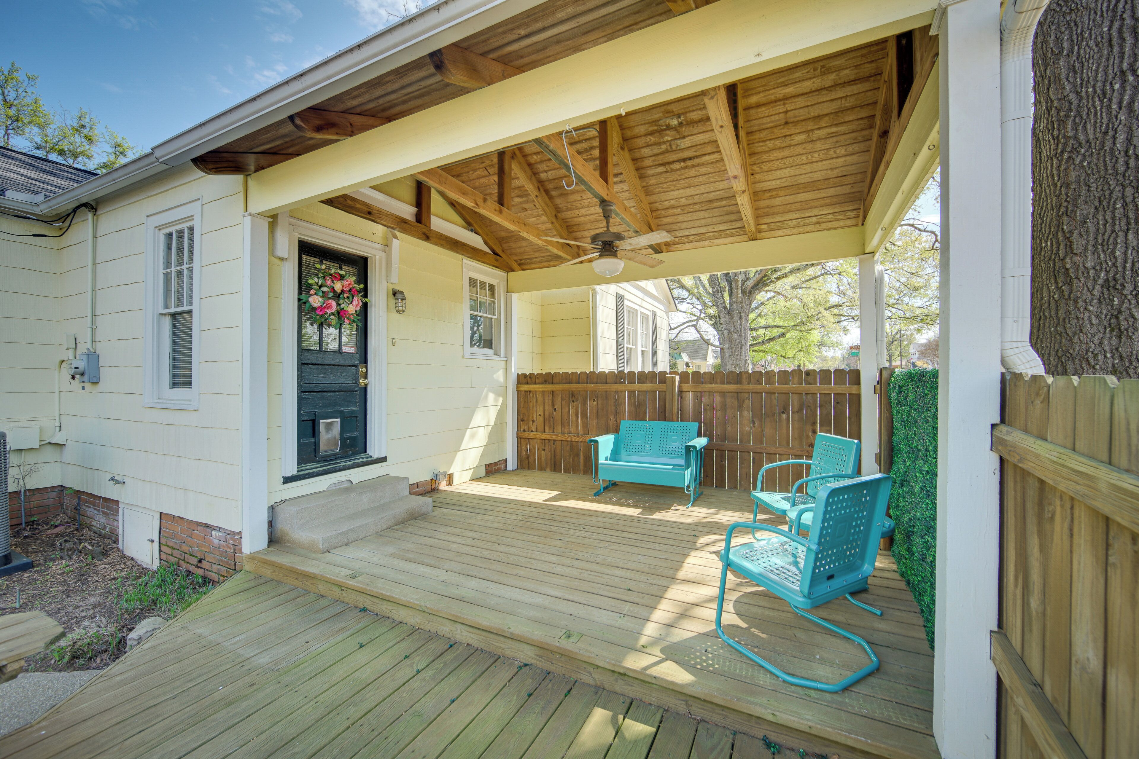A covered porch with wooden beams and a ceiling fan, two turquoise chairs, and a wooden fence in the background.