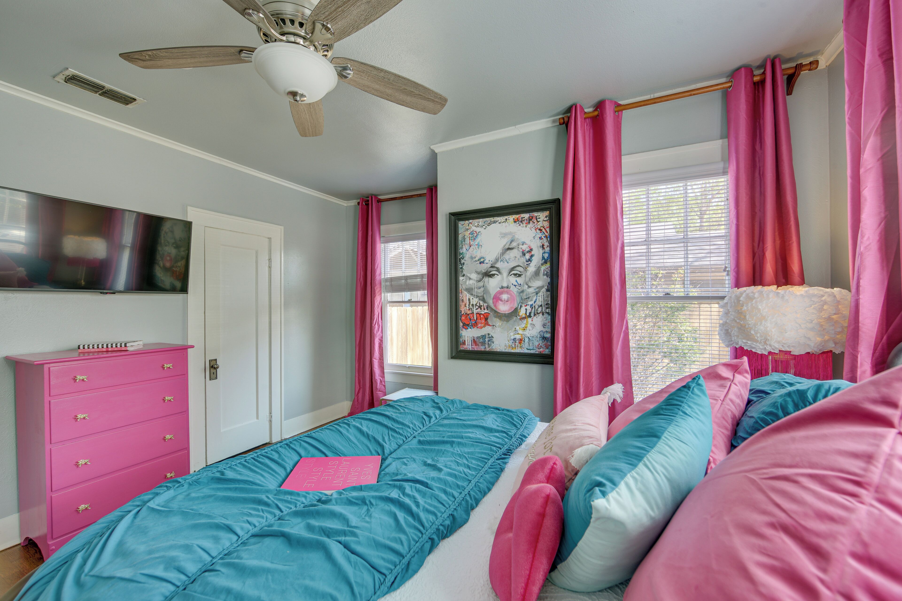 Un dormitorio con cama, cómoda, ventilador de techo y ventana con cortinas.
