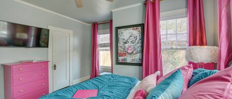 Un dormitorio con cama, cómoda, ventilador de techo y ventana con cortinas.
