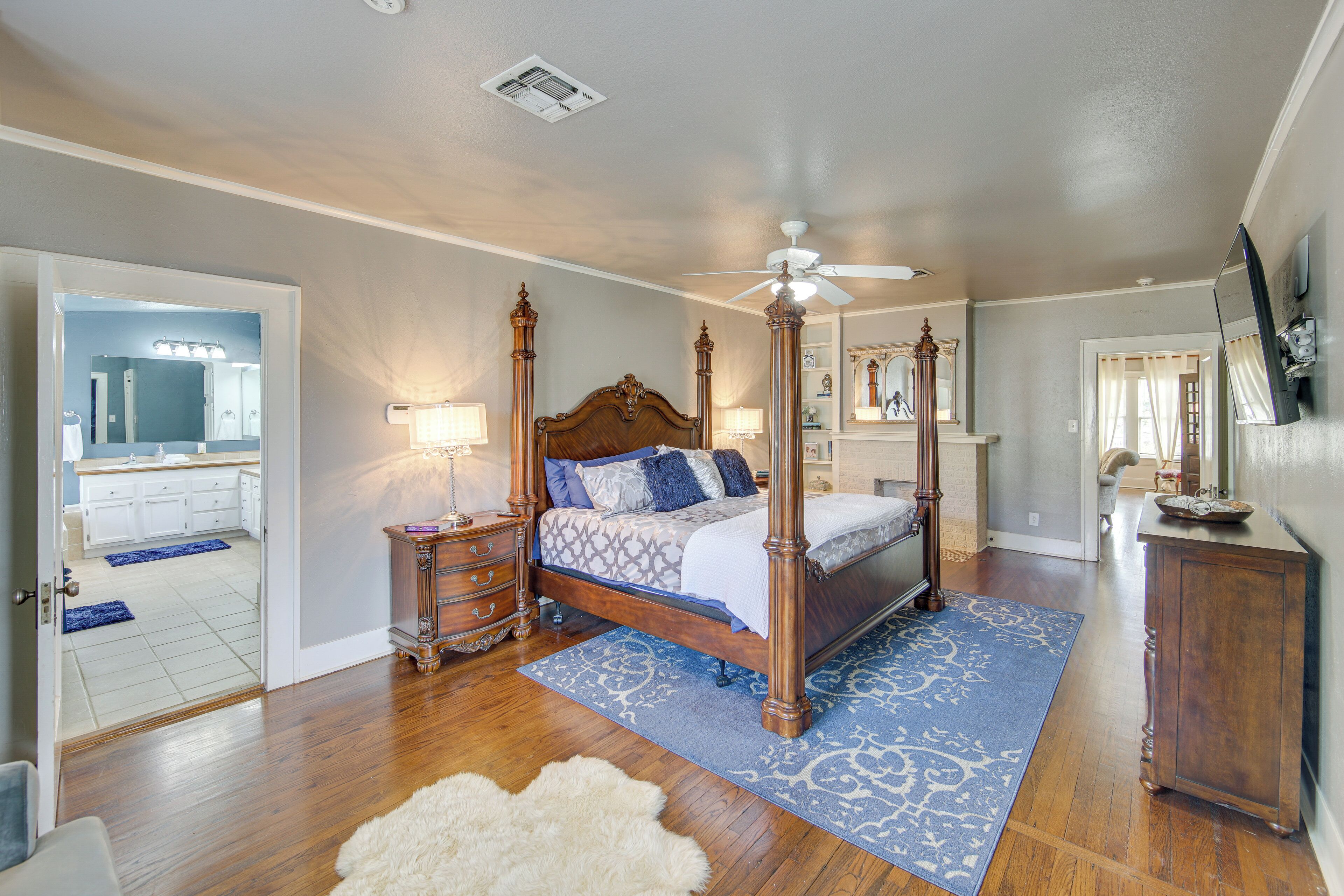 A spacious bedroom with a four-poster bed, wooden flooring, and a ceiling fan.