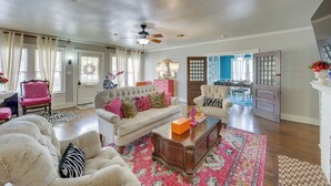 A spacious living room with a large sofa, two armchairs, and a coffee table. There is a ceiling fan, a rug, and a door leading to another room. - 'the Pink Azalea' - Tyler Home w/ Yard + Patio! (Tyler)