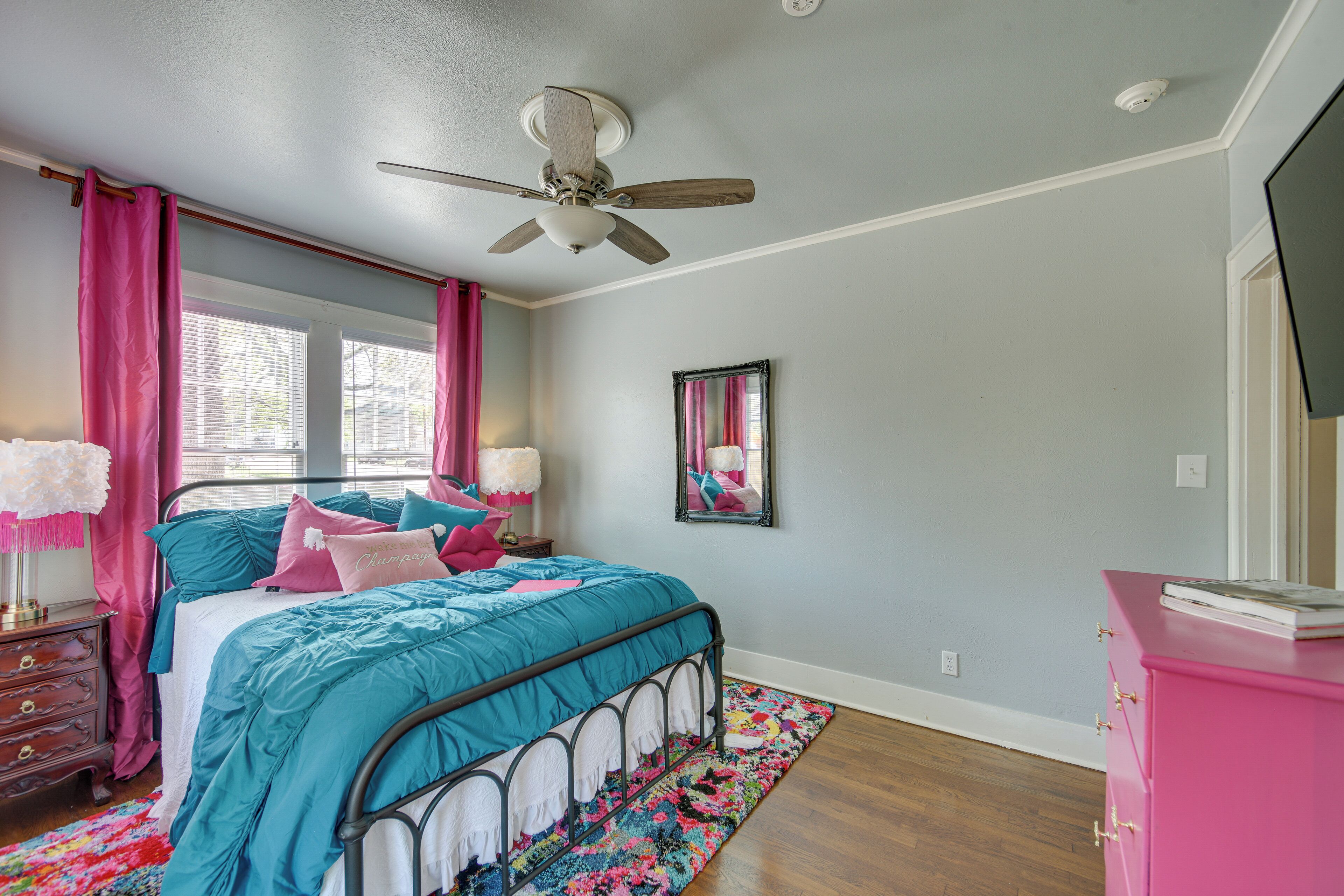 Une chambre à coucher avec un lit, un ventilateur de plafond, une commode et une fenêtre avec des rideaux.