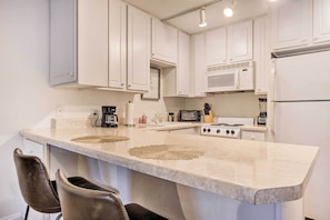 Une cuisine moderne avec des meubles blancs, un grand îlot central doté de deux tabourets, un four à micro-ondes, une cuisinière et divers appareils électroménagers.