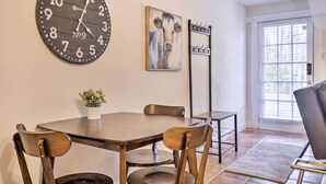 A dining area with a wooden table, four chairs, a clock, a painting, and a coat rack. - Ideally Located & Updated Chapel Hill Apartment! (Chapel Hill)