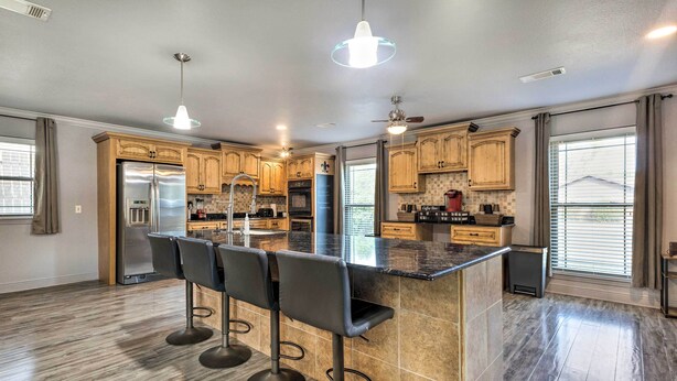 A modern kitchen with wooden cabinets, a stainless steel refrigerator, a large island with bar stools, and pendant lighting. - Inviting Gulfport Home w/ Private Pool & Yard (Gulfport)