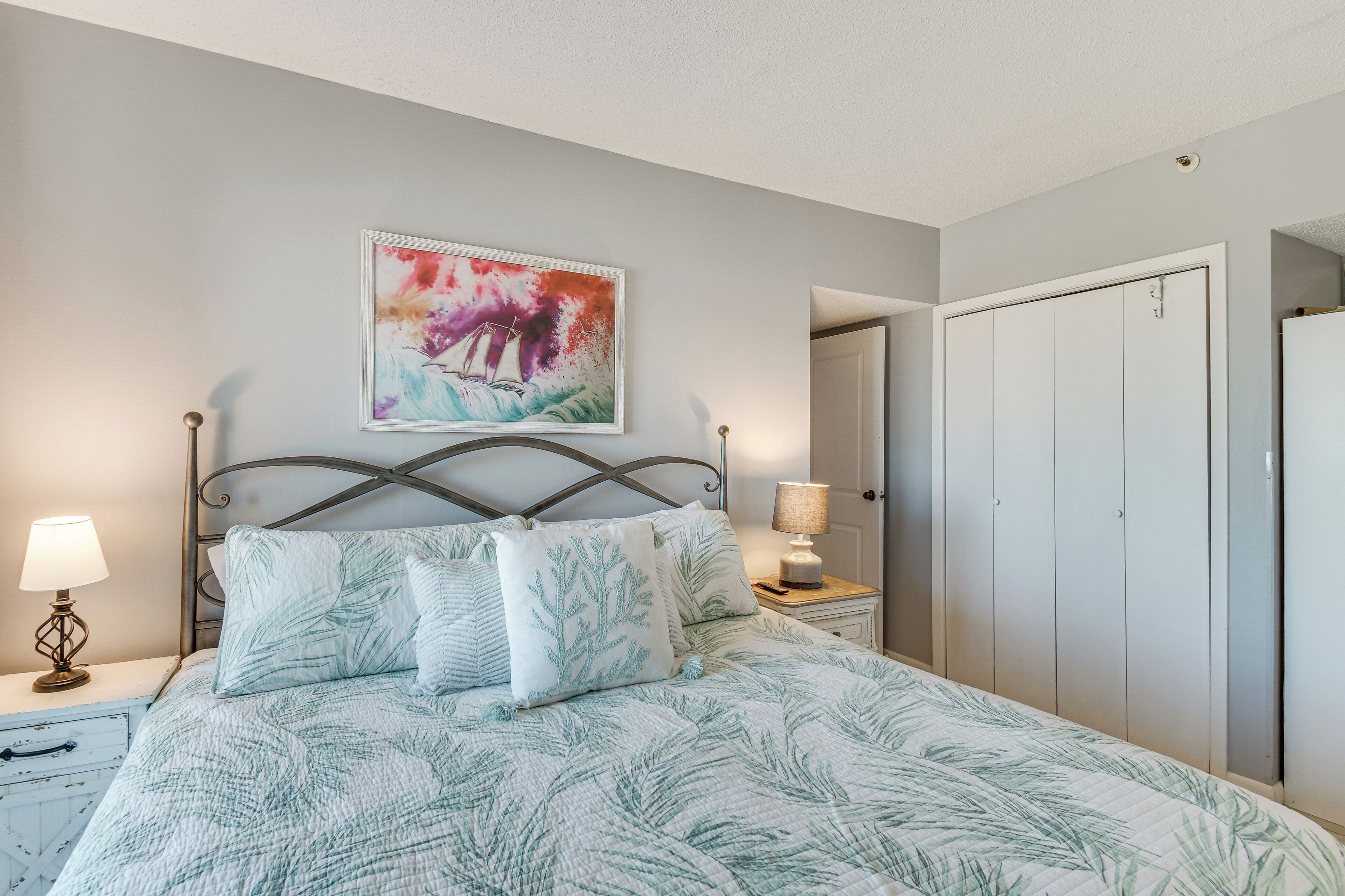 A bedroom with a bed, nightstands, a painting, and a wardrobe.