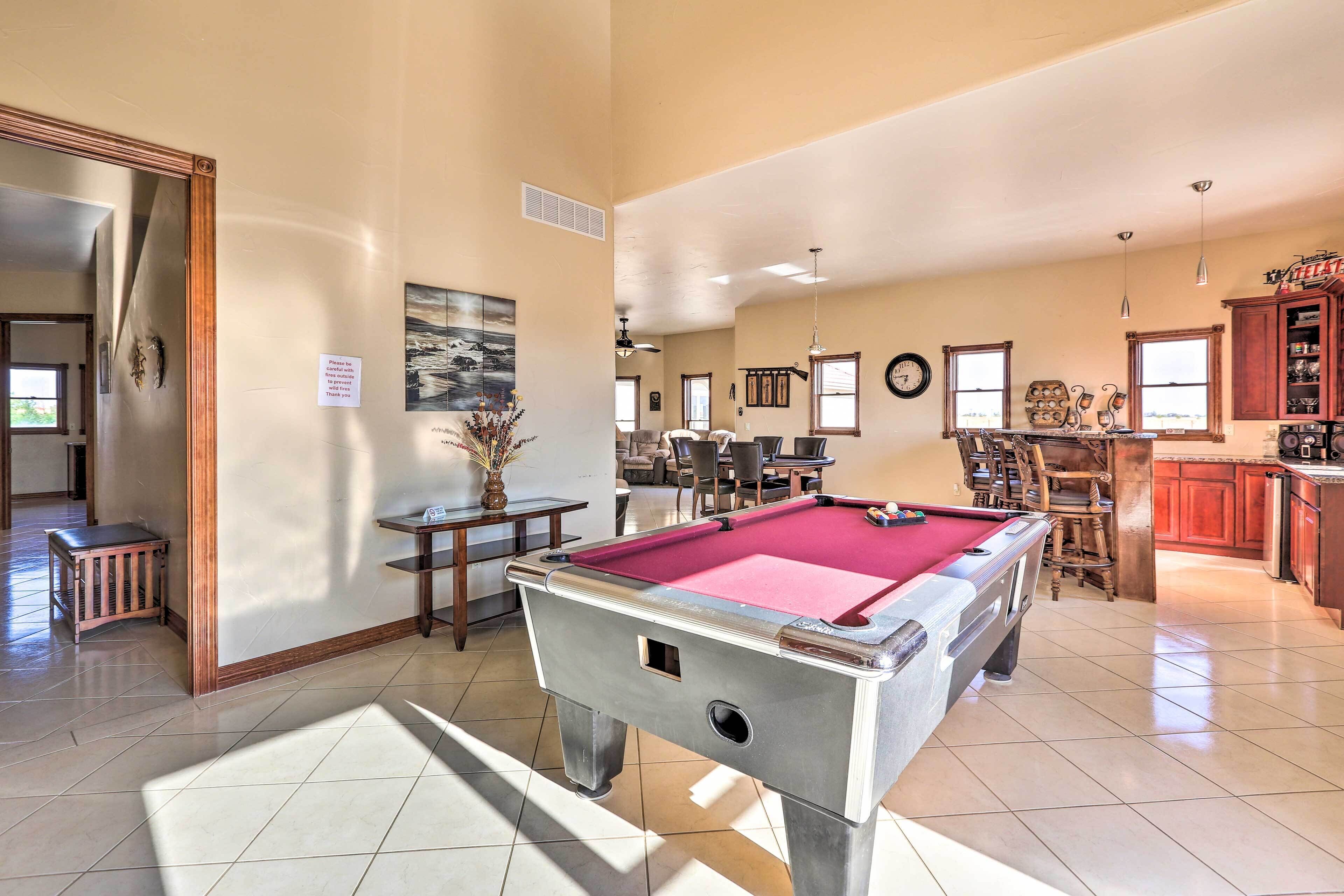 A spacious indoor area with a pool table, a dining area, and a kitchen.