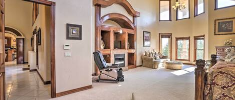 A spacious bedroom with a large bed, a sitting area with a sofa and ottoman, a fireplace, and a view of the outdoors.