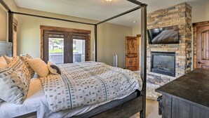 Un dormitorio con una cama con dosel, una chimenea de piedra y un televisor montado en la pared.