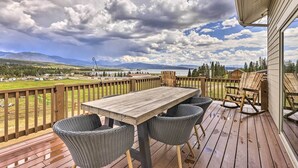 Una terraza de madera con una mesa y sillas, con vistas a un paisaje pintoresco con montañas y un lago.