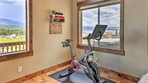 Una habitación con una bicicleta estática, un estante de madera con objetos, y vistas a un paisaje a través de amplias ventanas.